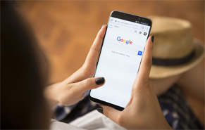 A woman's hand's holding a cellphone that has the Google homepage on it.