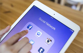 A hand touching the screen of an iPad that has the words "Social Network" on it.